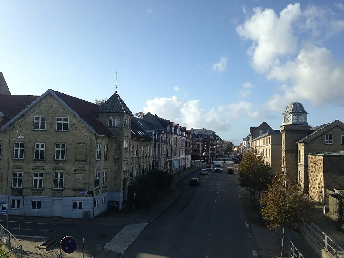A street in Aalborg with historic buildings and a few cars under a partly cloudy sky.