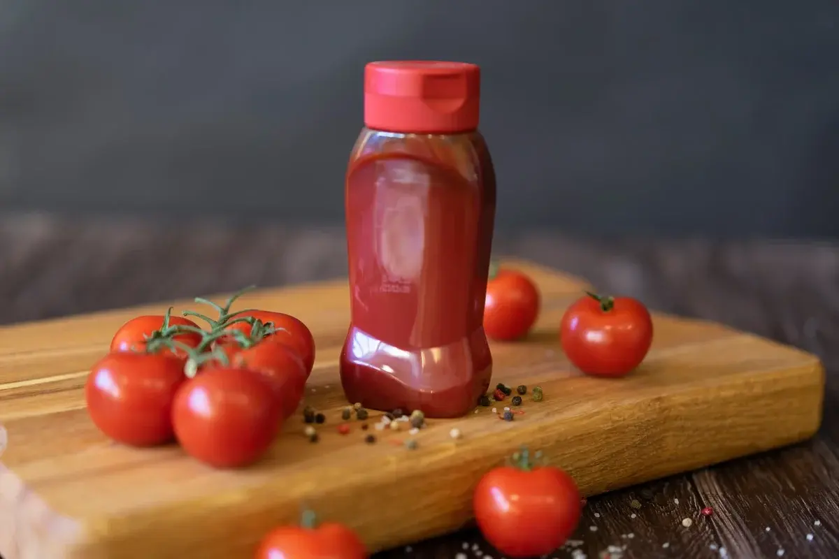 Ketchup bottle with tomatoes on a wooden board.