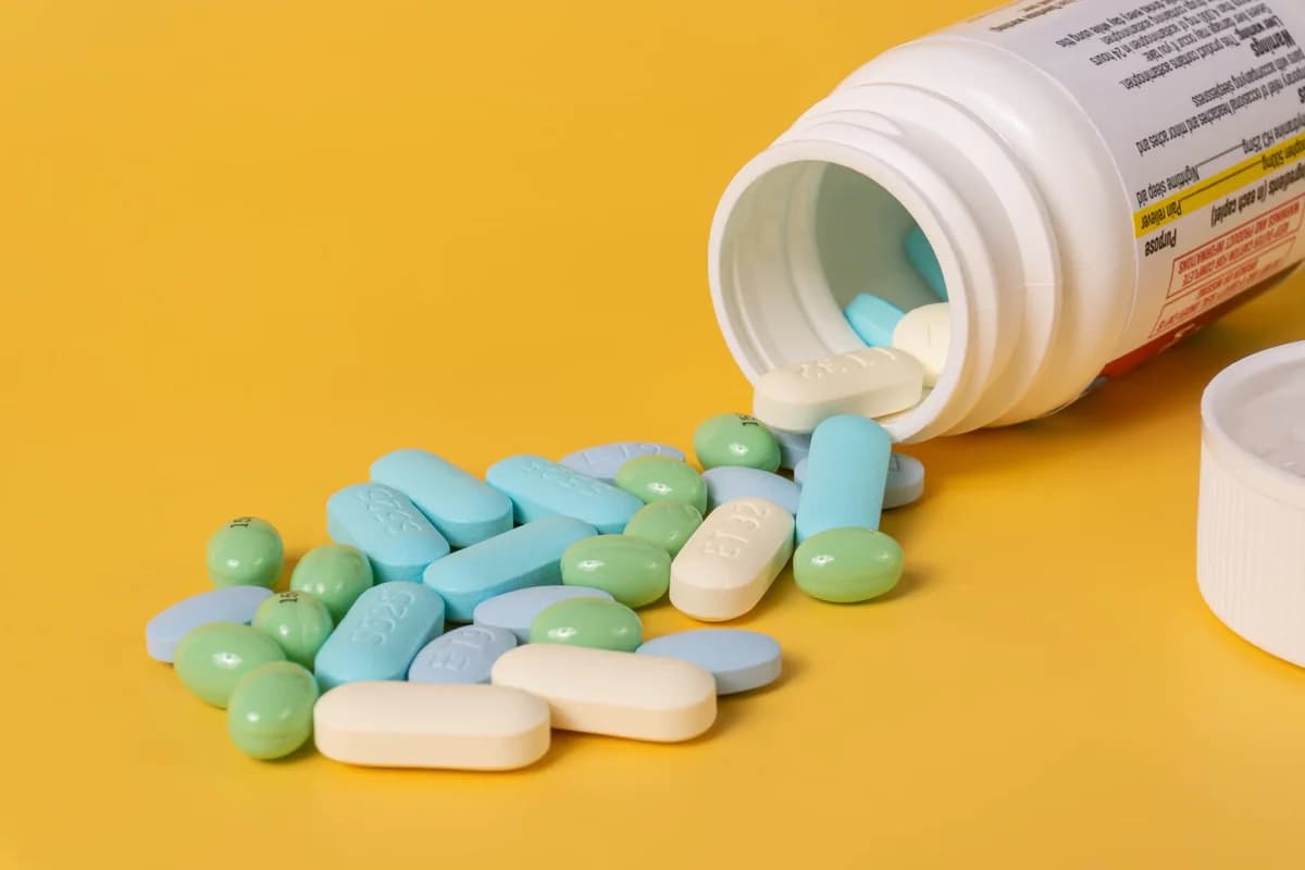 An open bottle spilling assorted pills onto a yellow background