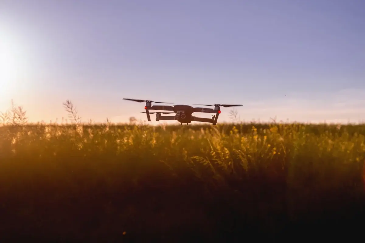 A drone flying over a field at sunset.