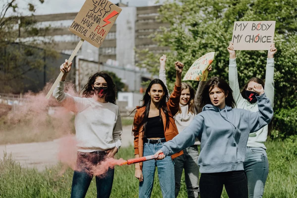 A group of women protest outdoors with signs and pink smoke.