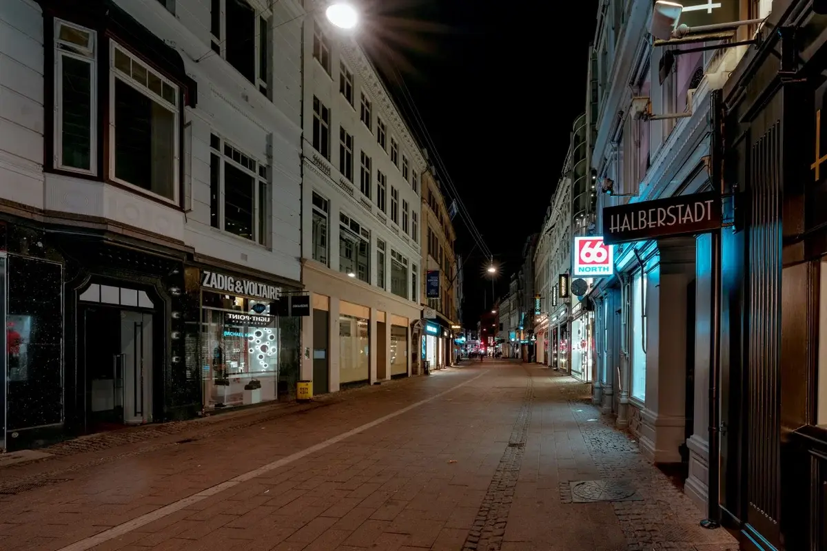 Empty Copenhagen street at night with lit shop windows and street lamps.