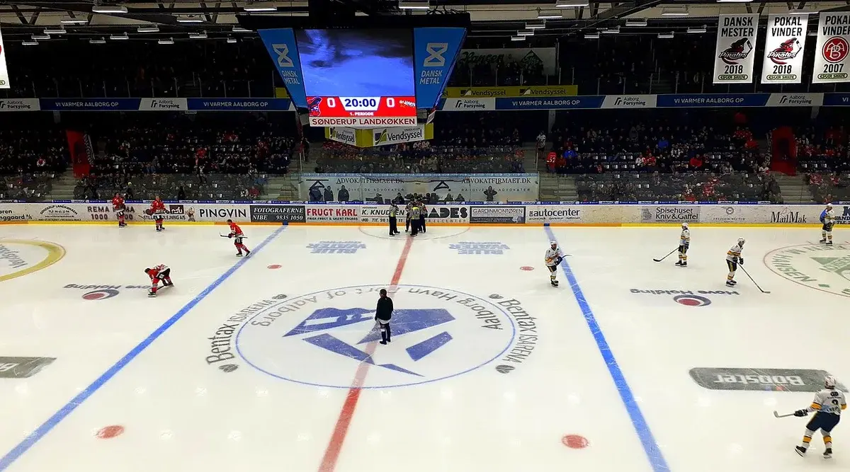Ice hockey players on the rink at Gigantium in Aalborg, Denmark, with the scoreboard showing 0-0 and 20:00.